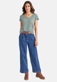 Olijfgroen t-shirt met korte mouwen, ontspannen pasvorm, gecombineerd met wijding blauwe jeans. Bruine riem met een decoratieve metalen gesp en bruine laarzen.
