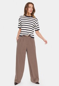 Haut en maille rayée crème et marine, associé à un pantalon large taille haute marron. Comprend une ceinture marron et des poches dans le pantalon.