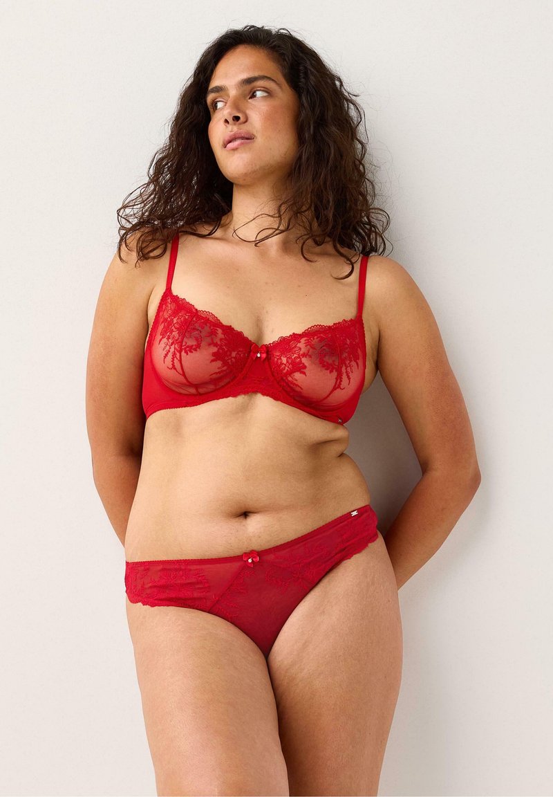 Červená krajková podprsenka a tanga set s květinovou výšivkou, průhlednými panely, nastavitelnými ramínky a malými dekoračními mašlemi na pásku.