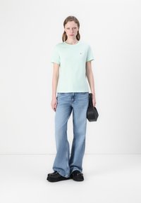 T-Shirt u mint zelenoj boji od pamuka s kratkim rukavima, uparen s svijetloplavim trapericama u obliku zvona. Crna torba sa strukturiranim dizajnom i cipele na platformu.