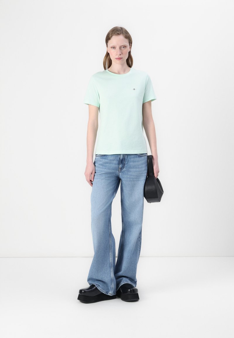 Mintgroen katoenen T-shirt met korte mouwen, gecombineerd met lichtblauwe flared jeans. Zwarte handtas met een gestructureerd ontwerp en platform schoenen.