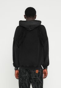 Μαύρο φούτερ με κουκούλα, με ριμπ μανσέτες και τελείωμα, υφασμένα ραφές στην πλάτη και άνετη εφαρμογή. Συνδυασμένο με σκούρο παντελόνι με σχέδιο.