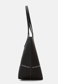 Czarna, trójkątna torebka wykonana z teksturowanej skóry. Posiada długie uchwyty oraz białe logo "Calvin Klein Jeans" z boku.