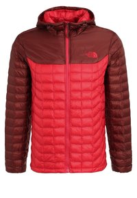Giacca a vento imbottita rossa e marrone scuro con zip frontale, cappuccio e texture trapuntata. Presenta un logo sul petto e un design a colori bloccati.