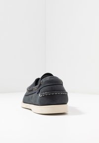 Dark blue leather boat shoe with white stitching, rubber sole, and metal eyelets. Features a low-profile design and rounded heel.