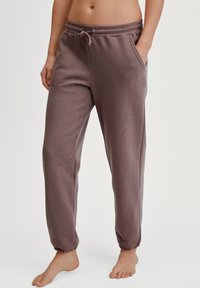 Weiche, mauve Jogginghosen mit einem elastischen Bund, Kordelzug, seitlichen Taschen und gerippten Knöcheln. Hergestellt aus einem dehnbaren Stoff, geeignet für die Freizeit.