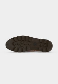 Semelle d'une botte avec des motifs de bande de roulement profonds en caoutchouc brun foncé, montrant des grips rectangulaires et en forme de croix pour la traction.