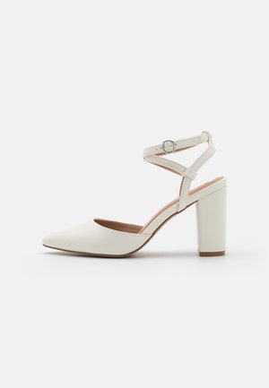 Zapato de tacón alto blanco con punta puntiaguda, material de cuero y tacón bloque. Cuenta con una delgada correa en el tobillo con un acento de hebilla circular.