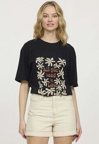 T-shirt en coton noir avec un design floral et la phrase "Tout ce dont vous avez besoin, c'est de l'amour" en rouge, associé à un short en denim de couleur claire.