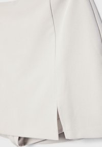 Približen posnetek svetlo bež tkanine z majhno režo in čistim šivom na robu oblačila.