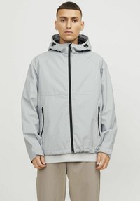 Hellgraue wasserdichte Jacke mit Kapuze, schwarzem Reißverschluss und seitlichen Taschen. Sie verfügt über ein strukturiertes Gittermuster und verstellbare Kordeln.