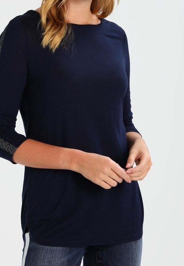 Mörkblå långärmad topp med rund halsringning, sidofickor och texturerade detaljer på axlarna, i kombination med jeans.