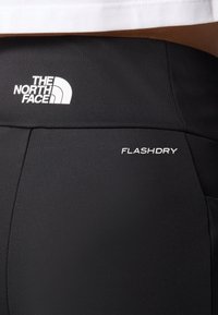 Svarta träningsshorts i mjukt material. Har vita logotyper: "THE NORTH FACE" och "FLASHDRY." Minimalistisk design utan mönster.