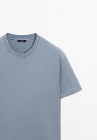 Světle modré bavlněné tričko s kulatým výstřihem, krátkým rukávem, hladkou texturou a jemným prošíváním podél výstřihu.