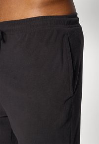 Zwarte fleecesweatpants met een elastische tailleband, zijzakken en een gladde textuur. Het ontwerp biedt comfort en bewegingsvrijheid.