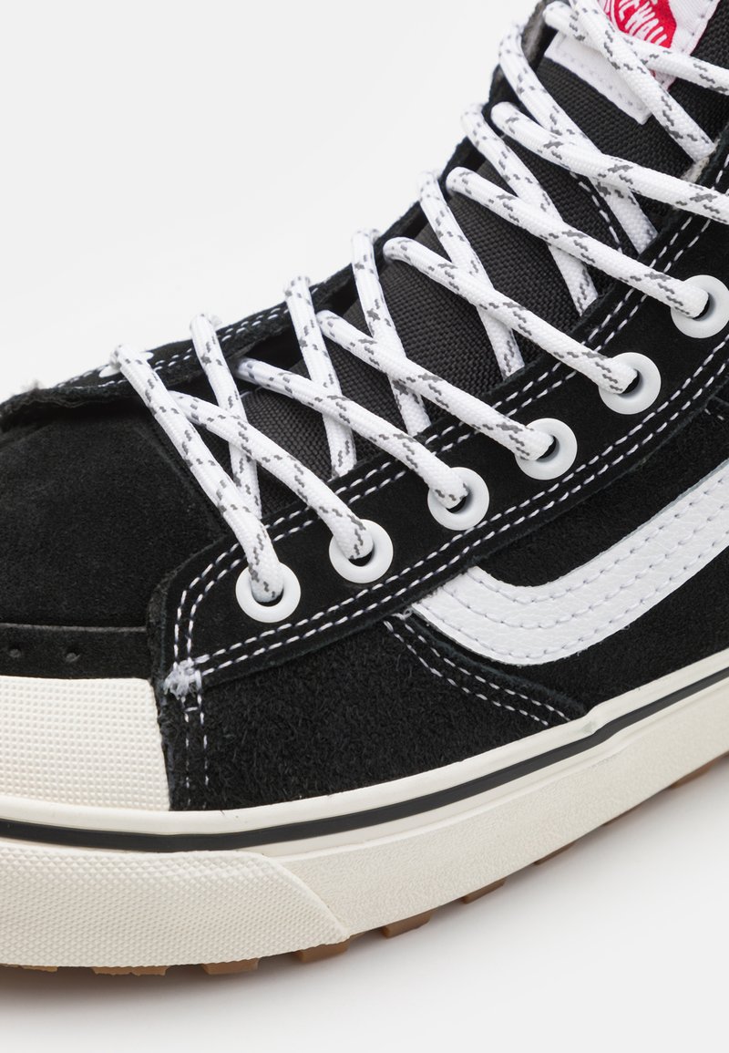 Czarne zamszowe sneakersy z białymi sznurowadłami, gumowym noskiem i kontrastującym białym paskiem po boku. Posiadają teksturowany materiał oraz niskoprofilowy design.