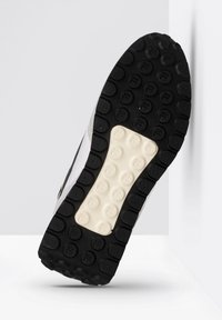 Sole di sneaker in gomma nera con motivo di battistrada circolare, caratterizzata da una sezione intermedia di colore crema e dettagli bianchi sui bordi superiori.