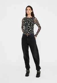 Bluză neagră cu mâneci lungi, cu buline albe și nod în față. Asortată cu pantaloni negri din denim, cu talie înaltă. Cizme negre de gleznă cu accente cu ținte.