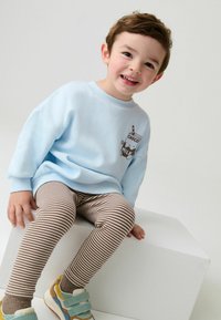 Svijetloplavi dukserica s grafikom čokoladnog mlijeka, uparen s smešnim i bijelim prugastim tajicama i šarenim tenisicama.