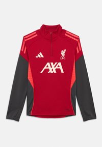 Punane sportlik pullover kõrge kraega, pikkade varrukate ja mustade külgpaneelidega. Oman valget logo ja teksti ning punaste ja mustade aktsentidega.