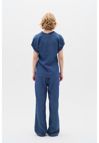 Džínový outfit skládající se z přiléhavého topu s nafouklými rukávy a kulatým výstřihem, doplněný volně střiženými rovnými nohavicemi v jednotném modrém odstínu.