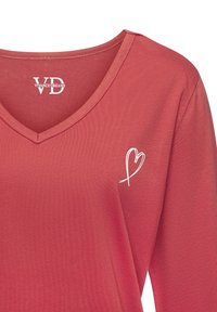 Rotes V-Ausschnitt-Oberteil aus weichem Stoff, mit einem weißen Herzdesign auf der linken Brust. Einfacher, lässiger Stil mit langen Ärmeln.
