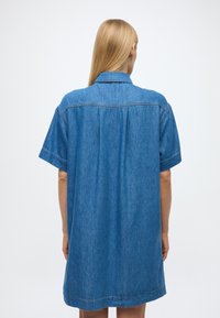 Džínsové šaty-košeľa s krátkymi rukávmi, svetlomodrej farby a voľného strihu. Má špicatý golier a zadný záhyb pre doplnenie dizajnu.