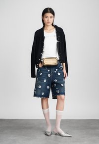 Traper šortsevi s bijelim cvjetnim vezom, u kombinaciji s bijelom majicom i tamnoplavim kardiganom. Srebrne cipele s šiljastim nosom, neprozirne bijele čarape i torba preko tijela.