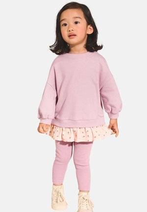 Felpa lavanda con maniche a palloncino, indossata sopra una gonna rosa con punti metallici, abbinata a leggings rosa coordinati e scarpe bianche.