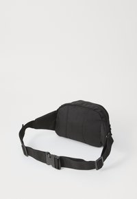 Fanny pack preta em tecido com fecho de zíper, design acolchoado, alça ajustável e fecho de plástico. Forma compacta sem padrões visíveis.