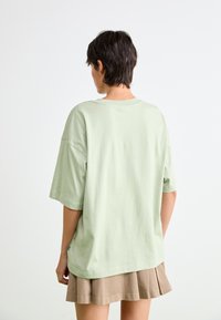 T-shirt oversize vert clair en coton doux, avec des manches courtes et un col rond, associé à une jupe plissée beige.