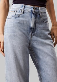Jeans in denim azzurro chiaro con vita alta, gamba dritta e una leggera sfumatura sbiadita. Presentano una chiusura con bottone e tasche frontali.