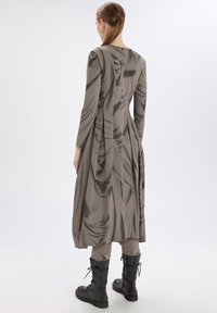 Vestido largo y ajustado de color gris con tela fluida, que presenta texturas drapeadas y un cuello alto. Lleva botas negras con cordones.