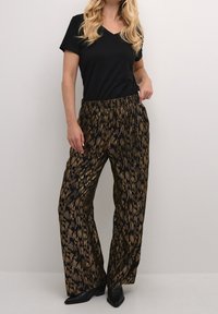 Väljämmät mustat housut, joissa kullan ja pronssin abstrakti kuvio, yhdistetty istuvaan mustaan V-kaulaiseen t-paitaan ja mustiin korollisiin kenkiin.