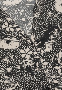 Sort og hvid mønstret stof med blomster- og prik-mønstre; har en V-udskæring og to sorte knapper til lukning.