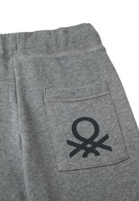 Graue Sweatpants mit elastischem Bund und einer Gesäßtasche, auf der ein schwarzes abstraktes Logo aufgedruckt ist.