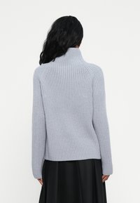 Maglione grigio chiaro a costine con colletto alto e maniche aderenti, caratterizzato da una linea dritta sull'orlo e una superficie testurizzata.