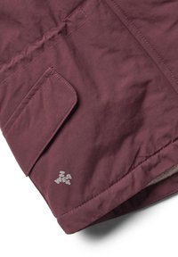 Bordeauxfarbener Jackenbereich mit einer Klapptasche. Merkmale sind sich kreuzende Nähte und ein kleines weißes Logo. Die weiche Innenverkleidung ist am unteren Rand sichtbar.