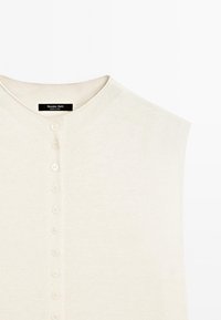 Haut sans manches en tricot couleur crème avec encolure ronde et une rangée verticale de petits boutons au centre devant.