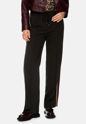 Black tailored pants with a relaxed fit, featuring a drawstring waist and contrasting side stripes in beige and red. Smooth texture.