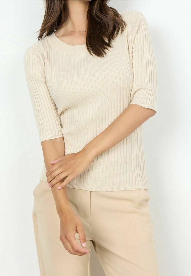 Top beige a costine in maglia con scollo tondo e maniche a gomito, abbinato a pantaloni beige chiaro. Tessuto strutturato, design aderente.