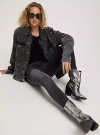 Szara dżinsowa kurtka na czarnej bluzce, zestawiona z szarymi obcisłymi dżinsami i metalicznie srebrnymi botkami na kostkę. Kręcone włosy i czarne kwadratowe okulary przeciwsłoneczne.