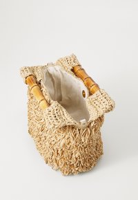 Geflochtene Strohtasche mit Bambusgriffen, strukturiert mit Fransen, offene Oberseite und Innenfutter aus hellbeigem Stoff. Kompakte zylindrische Form.