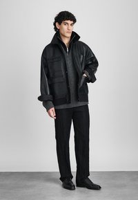 Black leather jacket with front pockets, grey knit sweater underneath, textured black pants, and black shoes, creating a layered look.