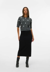 Šedý croptop se bílými puntíky, kombinovaný s černou, přiléhavou midi sukní. Černé kotníkové boty dokončují celkový vzhled.