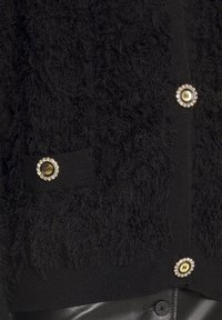 Schwarze strukturierte Strickjacke aus flauschigem Material, mit goldenen Knöpfen, die mit Strasssteinen verziert sind, und gerippten Kanten.