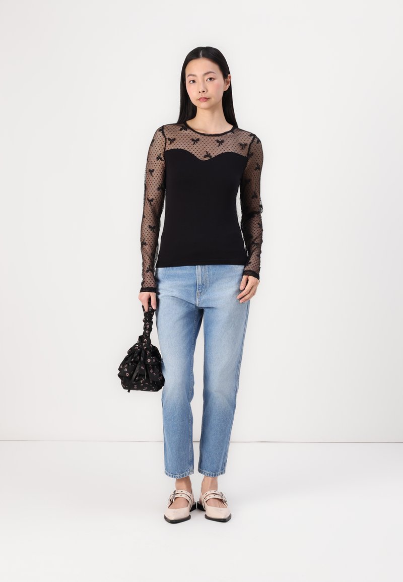 Maglia nera a maniche lunghe con rete trasparente a pois e decorazioni floreali, abbinata a jeans a gamba dritta blu chiaro e scarpe basse. Tiene una borsa nera.