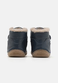 Botine de glezna din piele bleumarin cu o căptușeală moale din blană ușor maronie și curea cu velcro. Prezintă tălpi din cauciuc texturat bej, cu logo-ul brand-ului.