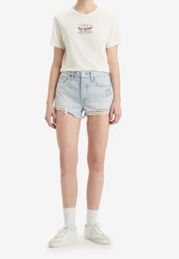 White cotton t-shirt featuring a colorful graphic design at the chest. Light blue denim shorts with frayed hem and mild distressing. White sneakers.