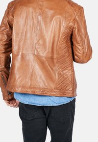 Braune Lederjacke mit tailliertem Design, strukturierter Oberfläche, schrägen Quiltakzenten auf dem Rücken und seitlichen Reißverschlusstaschen.